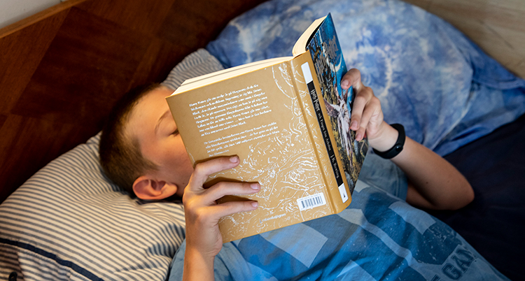 En pojke ligger i en säng och läser en bok.