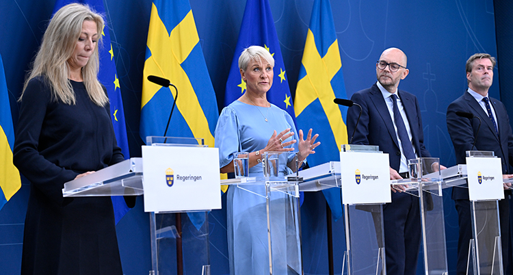 Fyra personer står på en rad med svenska flaggor bakom sig.