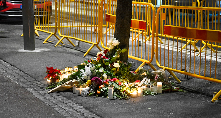 Det är mörkt ute. Människor har lagt blommor och ljus på en trottoar i Stockholm.