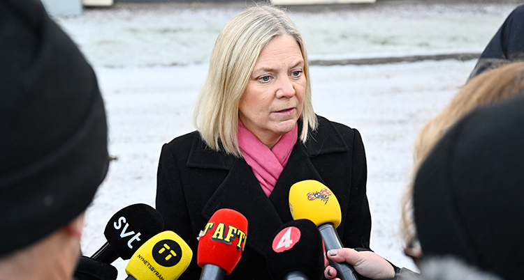 Hon står utomhus och pratar med en massa journalister som sträcker fram sina mikrofoner.