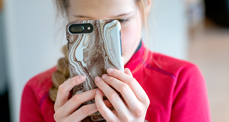 En flicka tittar påen mobil. Hennes ansikte syns inte.