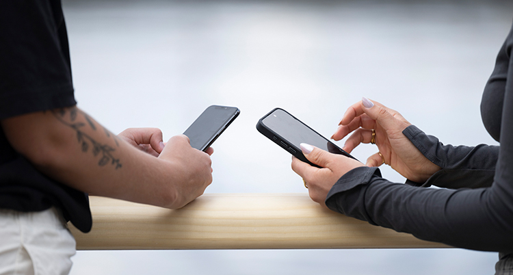 Två kvinnor håller i sina mobiler.