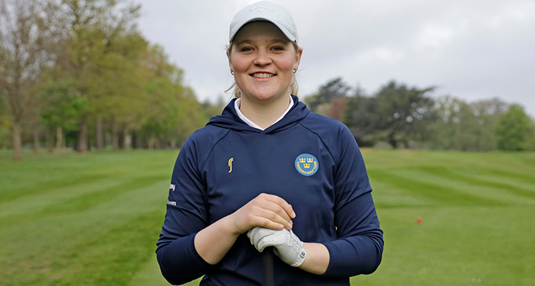 Hon har keps på huvudet. Hon har en handske på ena handen. Hon står på en golfbana.