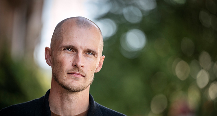 Han har inget hår på huvudet. Han ser allvarlig ut.