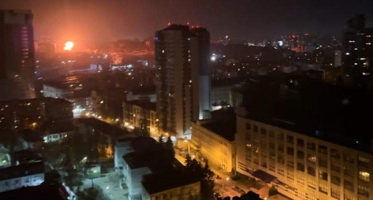 En stad på natten. Långt borta syns en explosion i mörkret.