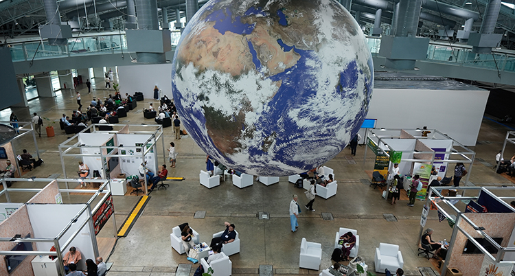 Folk sitter i en stor lokal. Ovanför dem svävar en stor jordglob.