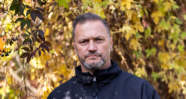 Han ser allvarlig ut. Bakom honom syns gula löv.