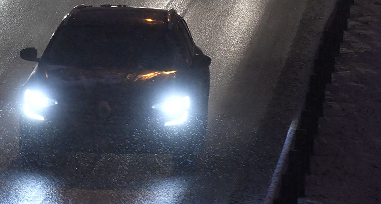 En bil kör i mörker. Lamporna på bilen är tända.