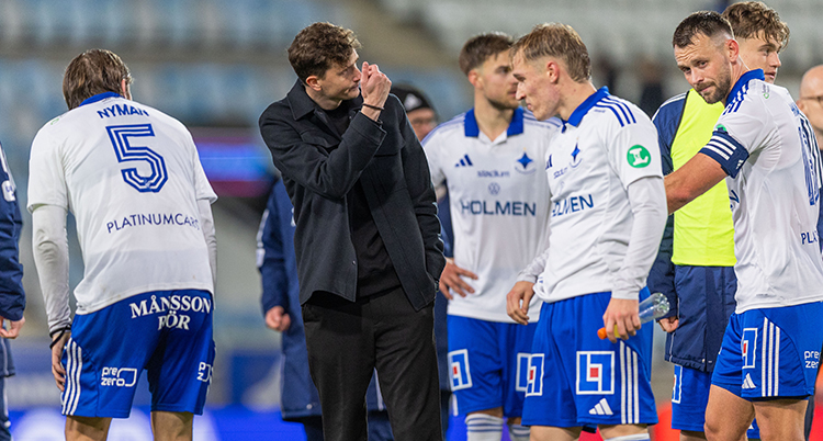 Några spelare och en tränare står i grupp på planen efter en match. De ser ledsna ut.