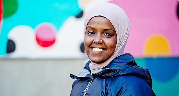 Hon ler och tittar in i kameran. Hon har en slöja över håret.