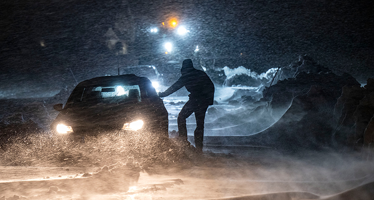 En man står utanför sin bil. Det är mörkt och det snöar.