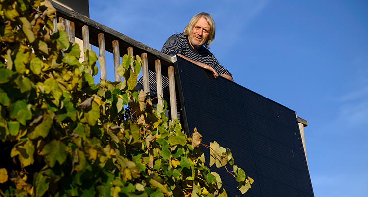 Han står på sin balkong. Solpaneler hänger ner på räcket.