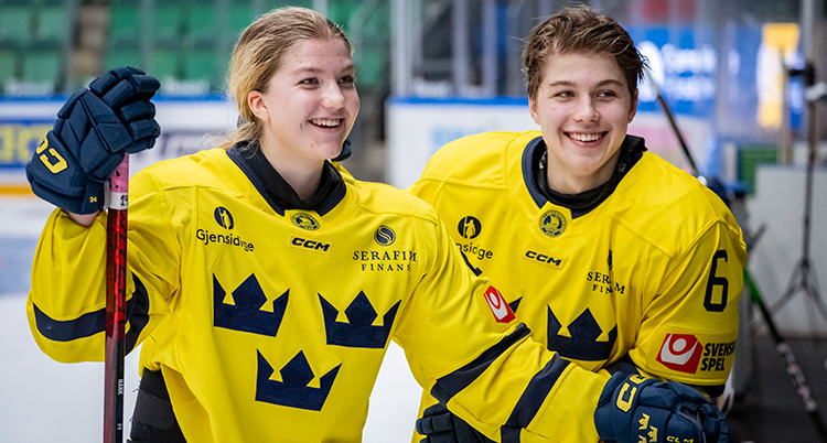 De står bredvid varandra. De har gula landslagströjor. Hon håller i en klubba.