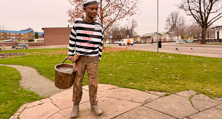 En staty ev ett barn har en randig tröja på sig. Statyn står på en gräsmatta.