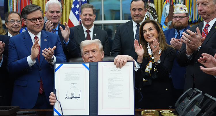 Han sitter vid ett bord och håller upp ett stort papper. Flera personer står omkring honom och applåderar.