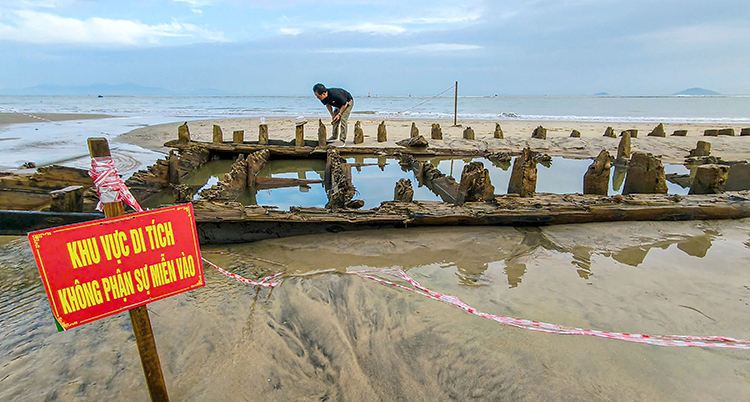 En person står vid vraket som är i sanden och vattnet.