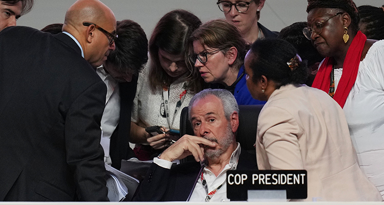 De står runt honom. Han sitter ned.