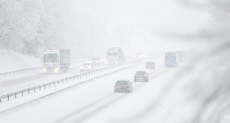 Bilar kör på vägen. Det är snö i luften och på vägarna.