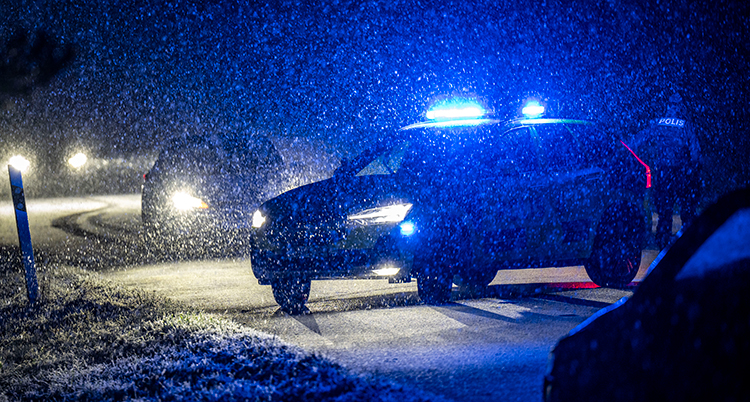 Blå ljus blinkar är tänd på bilen. Det är mörkt. Snö faller från himlen. Det är snö på vägen.