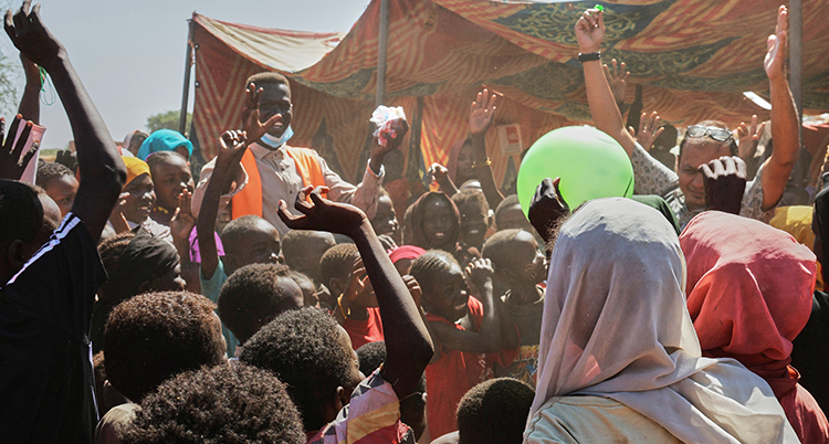 Människor står i ett läger av tält. De håller upp sina händer.