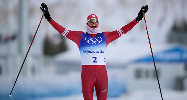 Han åker skidor. Han går i mål. Han sträcker armarna i luften och är glad.