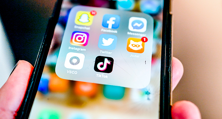 En hand som håller i en smart mobiltelefon. På skärmen syns ikoner för appar som Snapchat och Facebook.