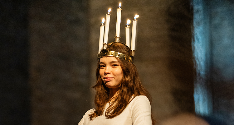 Hon tittar in i kameran och ler lite. Hon har en krona på huvudet med levande ljus.