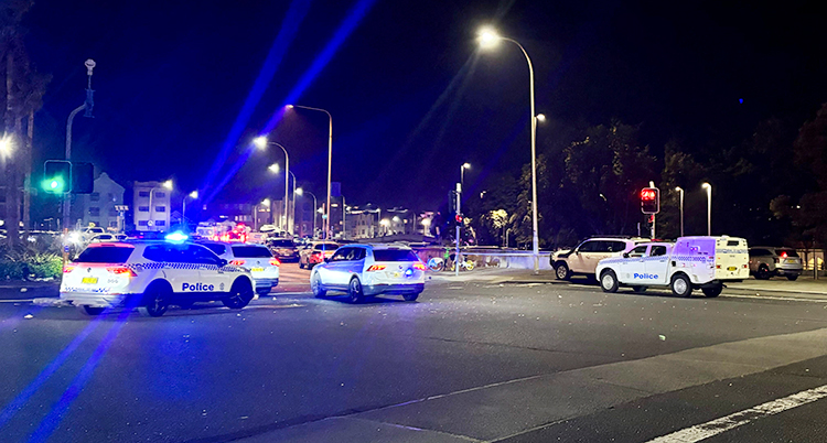 Det är mörkt ute. Flera polisbilar står på en gata i staden Sydney.