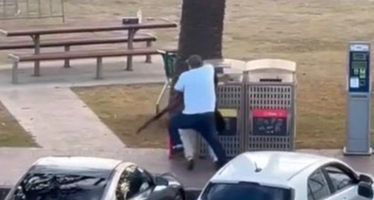 En man smyger fram bakom ett träd.