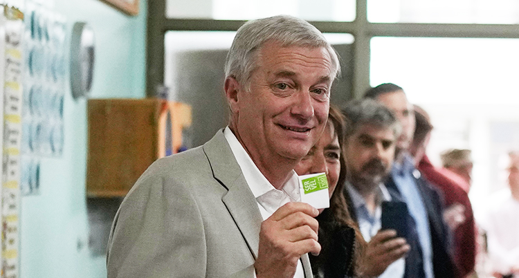 Han står i en vallokal. Han håller upp en liten lapp och ler.