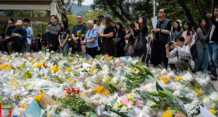 Människor står och tittar på massor av blommor som folk lagt ner.