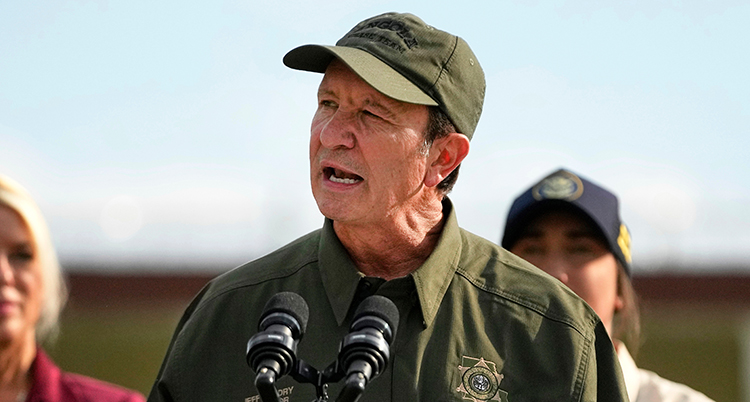 Han pratar i mikrofoner. Han har grön skjorta och grön keps.