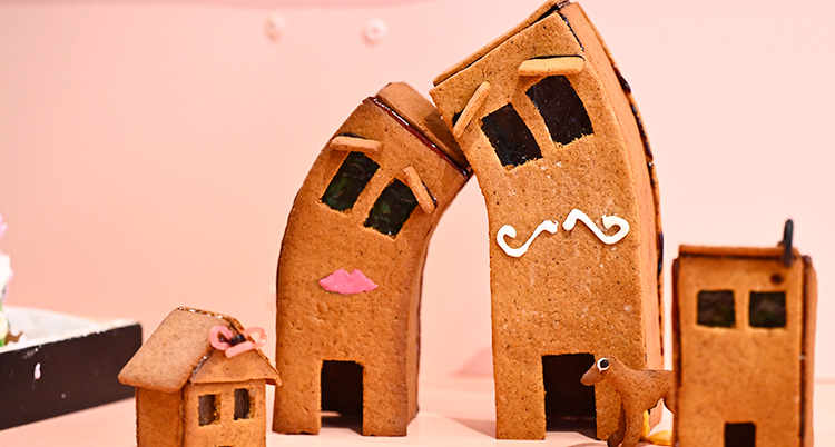 Två pepparkakshus som lutar sig mot varandra. Ett hus har en pussmun och det andra huset har en mustasch.