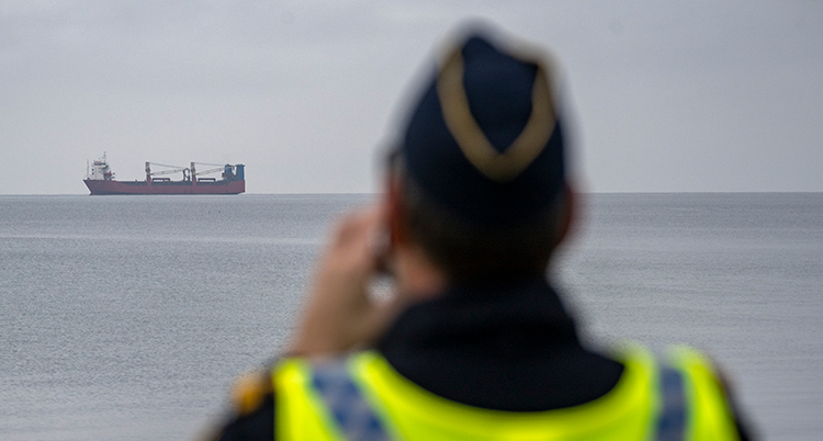 Ryggen på en man med gul väst. I bakgrunden syns ett stort fartyg.