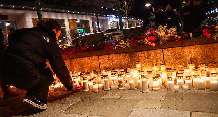 En person sitter vid många tända ljus på en öppen plats. Det är mörkt ute.