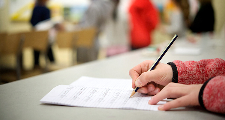 En elev sitter och skriver. Några andra elever är i bakgrunden.