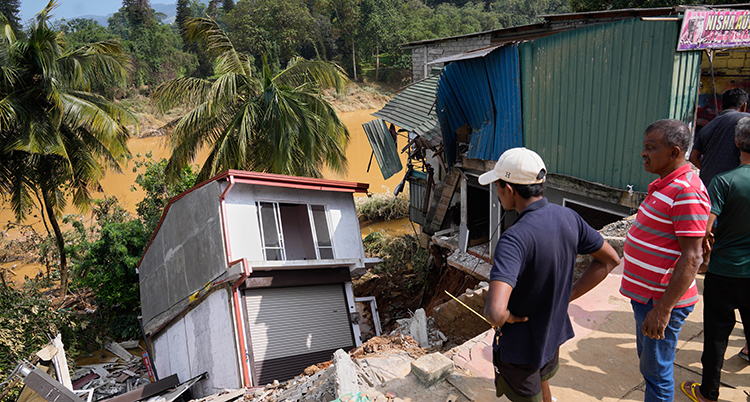 Människor tittar på ett hus som vält ner i en brant.