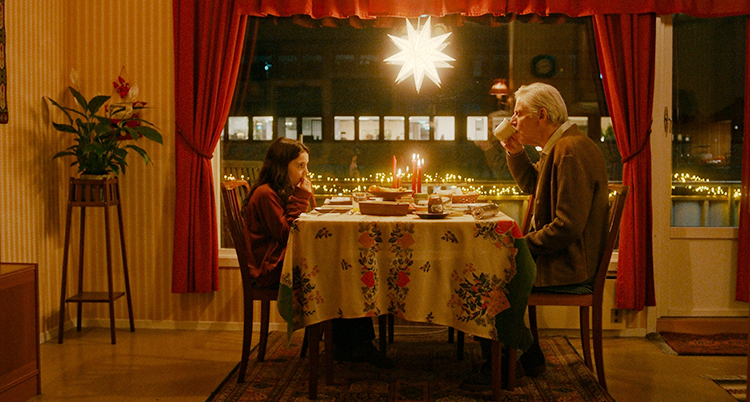 En flicka och en gubbe sitter mitt emot varandra vid ett köksbord.