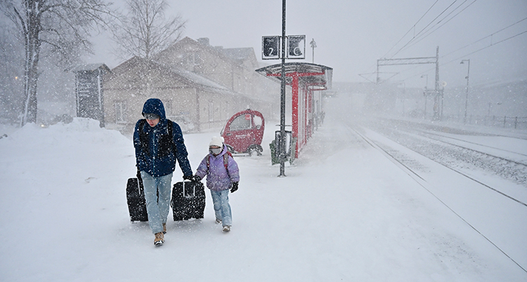 En vuxen och ett barn drar väskor på en tågperrong. Det snöar och blåser mycket.
