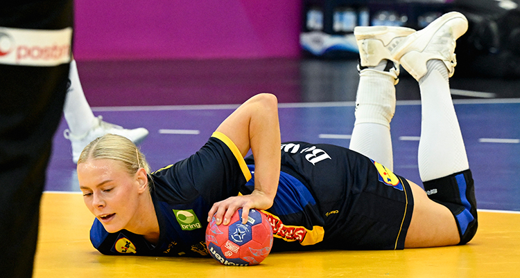 Hon ligger ner på mage på planen. Hon har bollen i ena handen.