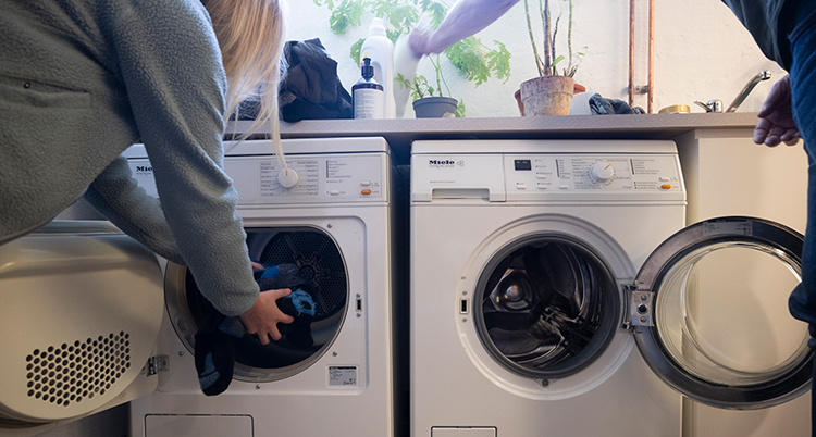Två personer lägger in saker i en tvättmaskin och i en torktumlare.