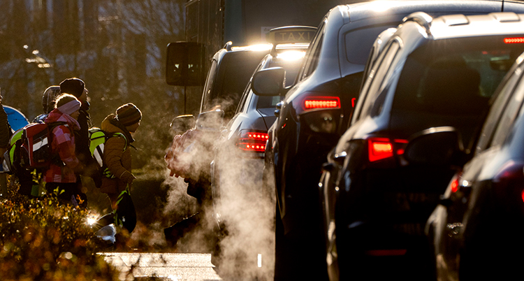 Barn går på en gata där bilar kör. Massor av gaser från bilarna syns i luften.