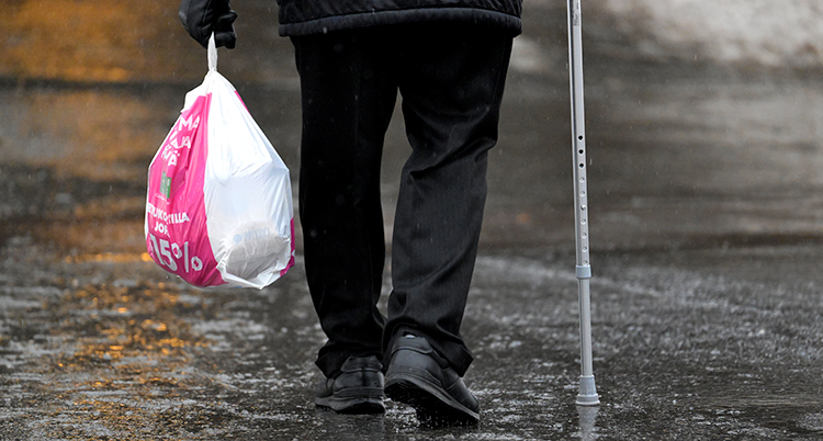 En person går på över isen. Personen håller i en krycka och en påse.