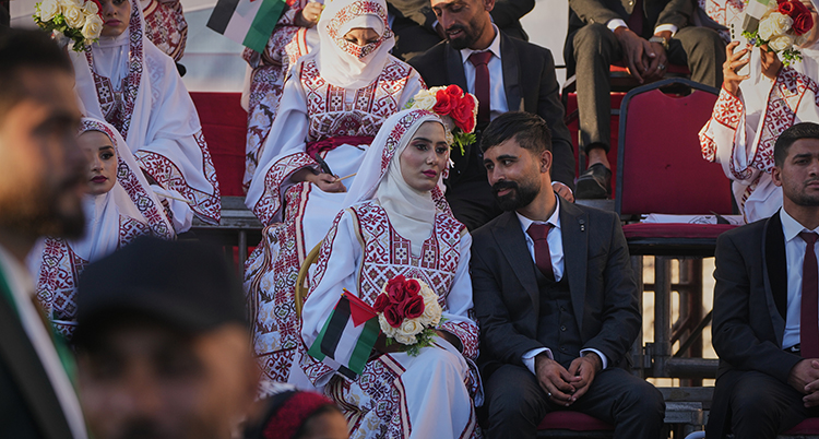 Hon har en dräkt med mönster och en sjal. Hon håller i en bukett blommor. Han har en kostym.