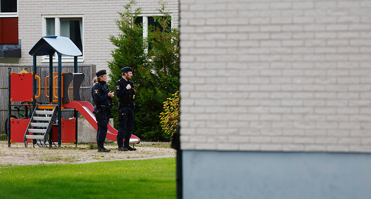 Två poliser står vid en lekplats på gården utanför lägenheten.