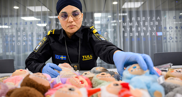 Hon har handskar på sig. Hon lyfter upp en av figurerna. De ser ut som små troll med vassa tänder.