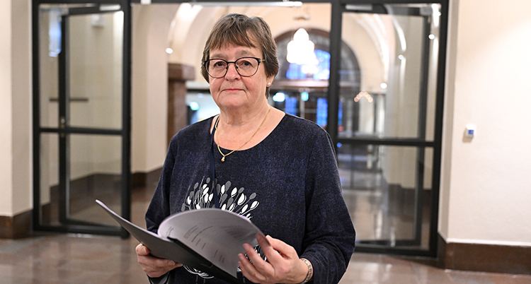 Hon står i en sal. Hon håller i ett papper.