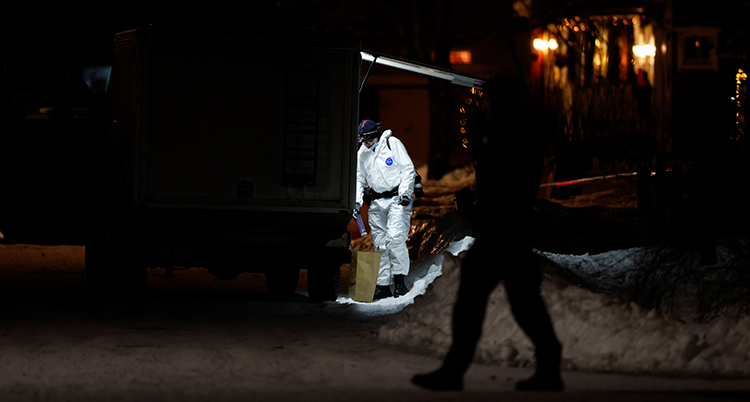 En person i vit dräkt jobbar för poliserna. Personen står bakom polisernas avspärrningar.