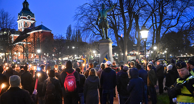 Folk står runt statyn. Vissa har facklor.