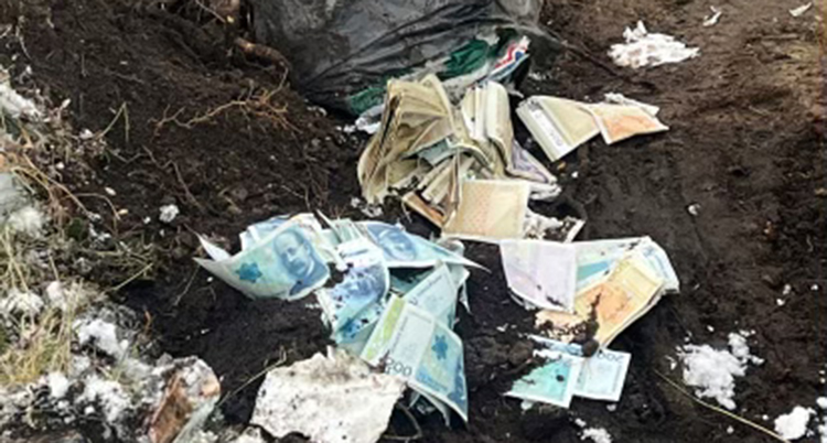 Sopsäcken ligger i jorden. Flera sedlar har trillat ur.